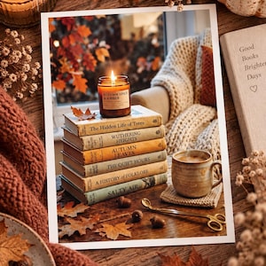 Op de afbeelding: Een stapel van zes vintage boeken met daarop een brandende kaars in een amberkleurig glas met het label Autumn Spice & Amber. Naast de boeken staan een keramische mok, een gouden lontknipper en verspreide bruine eikenbladeren.