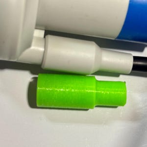 May include: Close-up of two plastic connectors, one white and one green. The white connector has a black wire attached to it. The green connector is smaller and has a textured surface.