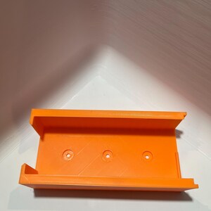 May include: Orange plastic 3D printed wall mount with three holes for mounting.