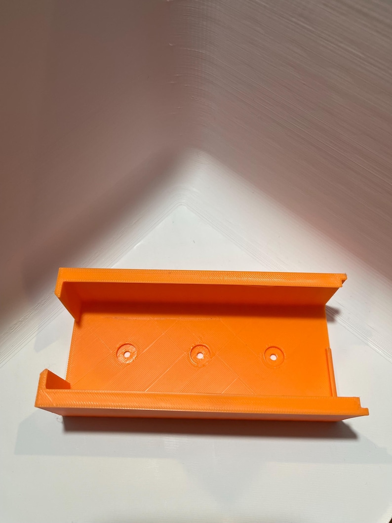 May include: Orange plastic 3D printed wall mount with three holes for mounting.