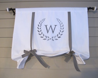 May include: White fabric window valance with gray accents. The valance features a gray laurel wreath design with the letter "W" in the center. Gray ribbons are tied into bows to gather the fabric.