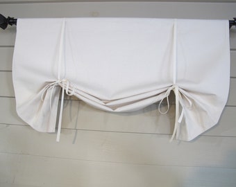 May include: A white fabric roman shade with two white ties on each side. The shade is hung on a black rod.
