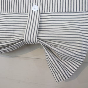 May include: A white and black striped fabric valance with a button detail. The valance is gathered at the center and has a curved bottom edge.