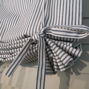 May include: Close-up of a fabric window treatment with a blue and white striped pattern. The fabric is gathered and tied with a matching striped ribbon. The design is reminiscent of a classic ticking stripe, suitable for home decor.