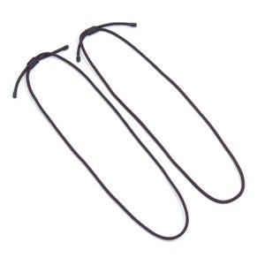 Puede incluir: Dos cordones ajustables de color marrón oscuro con nudos corredizos. Los cordones son finos y parecen estar hechos de un material tejido. Los cordones están sobre un fondo blanco.