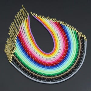 May include: A collection of multiple necklaces made from colorful, smooth, tubular cord material. Each necklace features a gold-tone metal lobster clasp and an adjustable chain link extender. The cords are solid colors including orange, yellow, pink, blue, green, brown, and gray, with a thin white reflective-style thread spiraling around each cord.