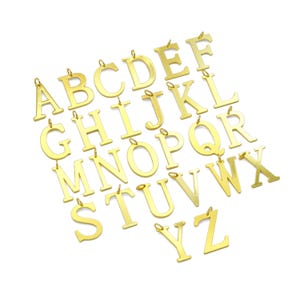 May include: A collection of gold-colored alphabet letter pendants, each with a small loop at the top for attaching to a chain or other jewelry. The letters are in a sans-serif font and are displayed against a white background.