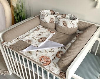 May include: A white crib with a brown and white patterned bedding set. The bedding includes a fitted sheet, a blanket, and a pillow. There are also two brown and white patterned bumper pads and two brown and white patterned storage baskets.
