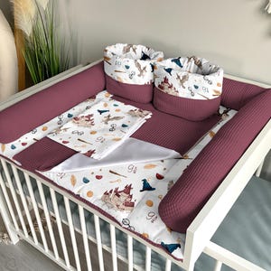 Peut inclure: Un lit bébé blanc avec un ensemble de literie de lit bébé bordeaux et blanc sur le thème d'Harry Potter. La literie comprend un drap-housse, un pare-chocs, une couverture et deux paniers de rangement. La literie de lit bébé a un imprimé du château de Poudlard, des hiboux et des lunettes.