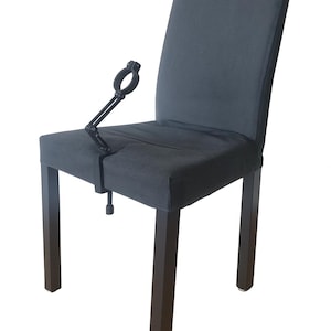 Könnte beinhalten: Ein dunkelgrauer, gepolsterter Stuhl mit einer schwarzen Metallfesselvorrichtung, die am Sitz befestigt ist. Der Stuhl hat dunkelbraune Beine und eine hohe Rückenlehne. Der Hintergrund ist weiß.