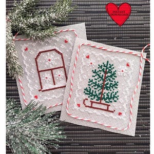 May include: Two cross-stitch patterns on white fabric with red and white string borders. The first pattern is a house with a window and snowflakes. The second pattern is a Christmas tree with a sled.