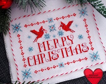 May include: A white cross-stitch fabric piece featuring the red text MERRY CHRISTMAS, two red birds, and blue snowflakes. The design is bordered by a red and white twisted cord, with a red heart icon in the corner labeled INSTANT DOWNLOAD.