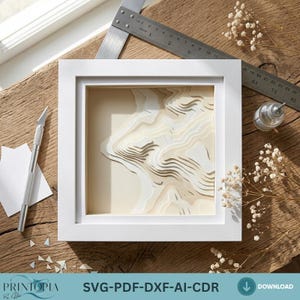 May include: A white framed 3D paper art piece depicting a topographic map. The artwork is layered with light beige and white paper, creating a sense of depth. A craft knife and ruler are visible, suggesting a DIY project. The text "SVG-PDF-DXF-AI-CDR" is at the bottom.