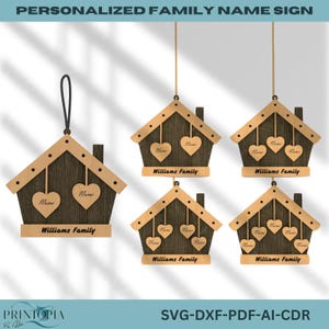 May include: Wooden house-shaped family name signs with heart-shaped cutouts. The signs are brown with a light brown roof and feature the family name "Williams Family" and the word "Name". Some signs hang from a black cord or gold chain.