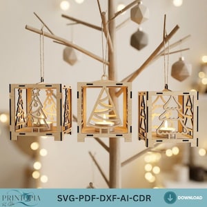 Op de afbeelding: Drie houten kerstboomlantaarns die aan een decoratieve boom hangen. Elke lantaarn heeft een uitgesneden boomontwerp en bevat een brandende kaars. De lantaarns zijn vierkant met gedetailleerde zijuitsparingen. De tekst "PRINTIOPIA" en "SVG-PDF-DXF-AI-CDR" staat onderaan.
