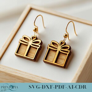 May include: A pair of gold-tone earrings with a wooden gift box design. The earrings are made of wood and have a laser-cut design. The gift boxes are detailed with a bow on top.  SVG-DXF-PDF-AI-CDR
