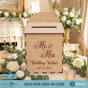 May include: A light-coloured wooden wedding card box with a slot on top. The box is engraved with "Mr. & Mrs. Wedding Wishes 24th.04.2023". The box is surrounded by white roses and greenery.