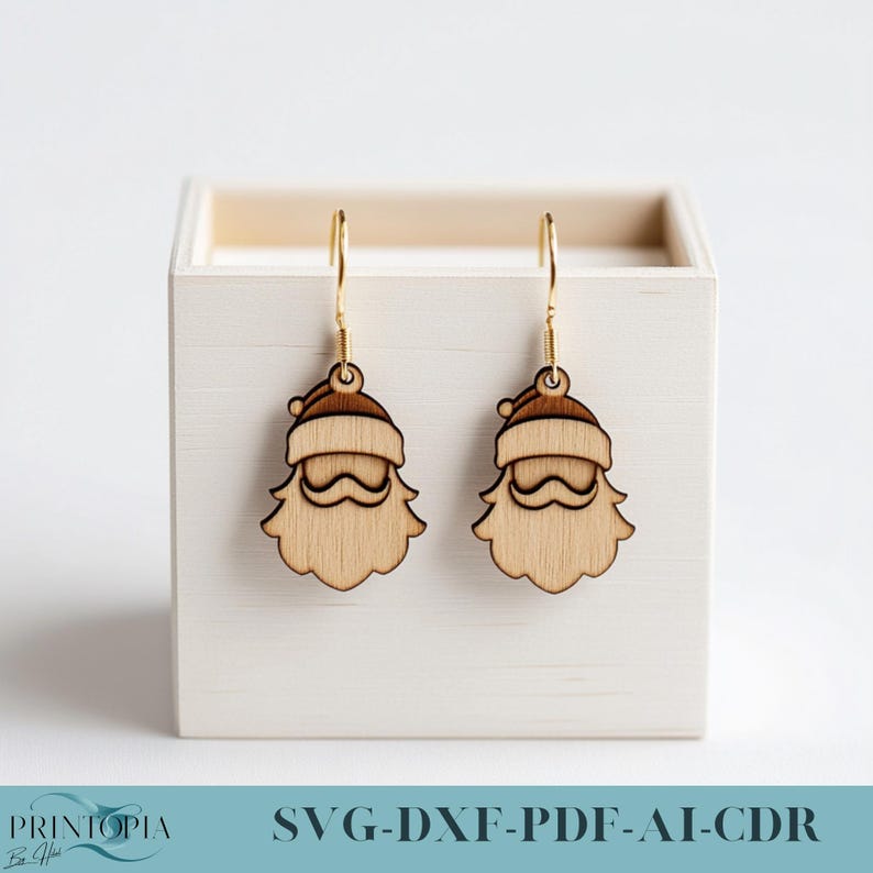 May include: A pair of wooden Santa Claus earrings with gold hooks. The earrings are in a white box with the text "SVG-DXF-PDF-AI-CDR" on the bottom.