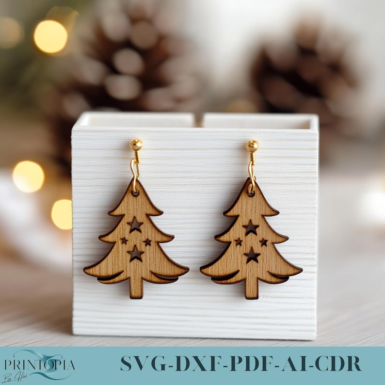 May include: A pair of wooden Christmas tree earrings with gold hooks. The earrings are in a white box with the text "SVG-DXF-PDF-AI-CDR" on the bottom.