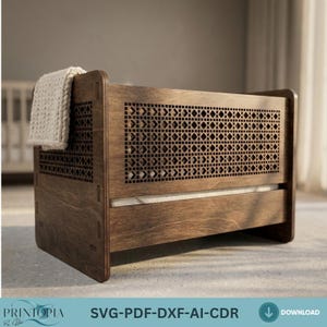 Puede incluir: Un cofre de almacenamiento de madera marrón oscuro con un patrón geométrico en el panel frontal. Una manta de color crema está drapeada sobre la parte superior. El cofre es rectangular. El texto "PRINTIOPIA" y "SVG-PDF-DXF-AI-CDR" son visibles.