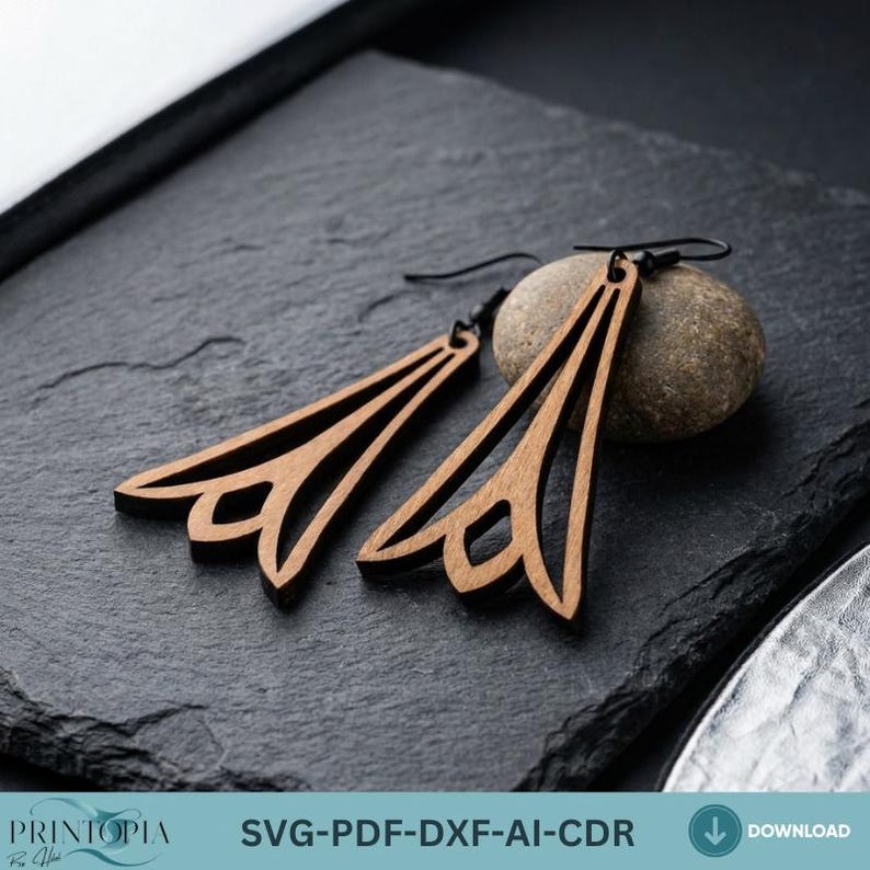 May include: A pair of wooden earrings with a geometric design. The earrings are a light brown color and have a triangular shape with a decorative cutout at the bottom. The earrings are displayed on a dark gray surface.