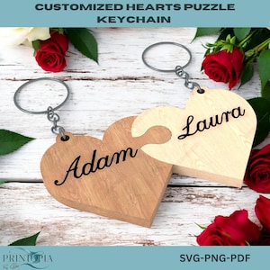May include: Two wooden heart-shaped puzzle pieces with the names "Adam" and "Laura" engraved on them. The pieces are attached to key rings and are shown against a white wooden background with red roses.