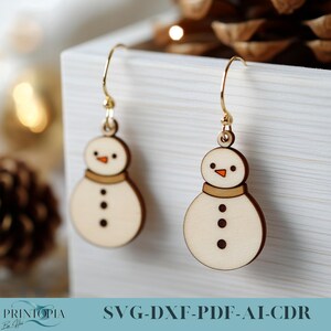 May include: A pair of gold dangle earrings with a wooden snowman charm. The snowman is white with a brown hat and black buttons.