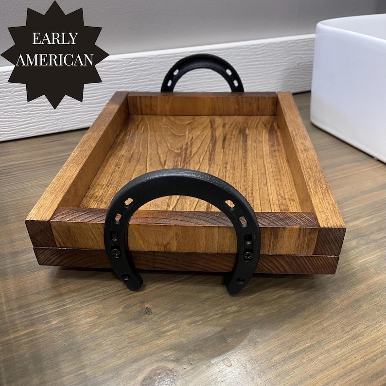 Puede incluir: Bandeja de madera rectangular con acabado marr&oacute;n oscuro. Cuenta con asas negras en forma de herradura. Las palabras "EARLY AMERICAN" est&aacute;n impresas en un gr&aacute;fico negro en forma de estrella. Aproximadamente 30 cm de largo.