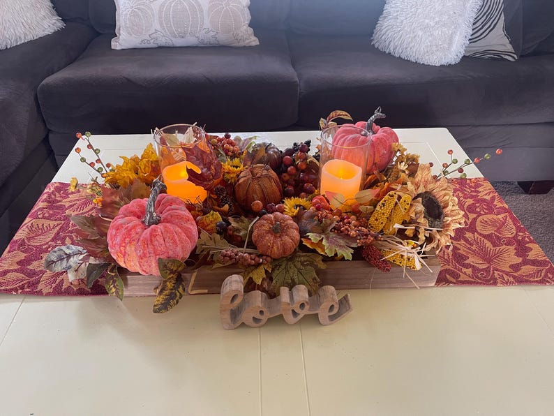 Puede incluir: Un centro de mesa con tem&aacute;tica oto&ntilde;al con calabazas, girasoles, bayas y hojas. Se incluyen dos velas encendidas en portavelas de cristal y un letrero de madera con la palabra "Love".