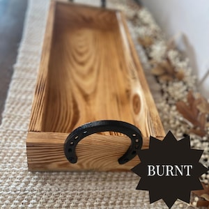 Puede incluir: Una bandeja rectangular de madera con acabado quemado y asa de herradura negra. La bandeja es de madera marr&oacute;n claro con vetas visibles y la palabra "BURNT" est&aacute; en una estrella negra.