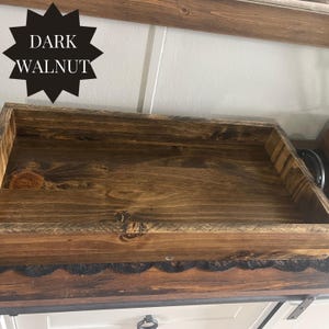 Puede incluir: Una bandeja de madera te&ntilde;ida de nogal oscuro con forma rectangular. La bandeja tiene vetas de madera visibles y un acabado oscuro. El texto "DARK WALNUT" se muestra en forma de estrella negra. La bandeja es probablemente para uso decorativo o funcional.