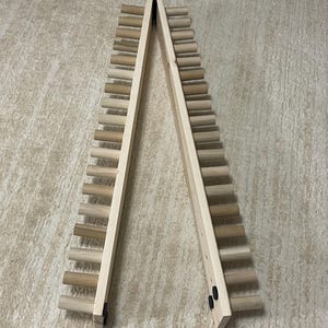 May include: A wooden wine rack with a ladder-like design. The rack is made of light-colored wood and features multiple horizontal dowels for holding wine bottles. The two sides are connected at the top with a hinge, allowing it to stand upright.