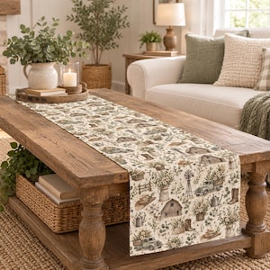 May include: A rectangular table runner featuring a repeating pattern of farm-themed illustrations including barns, vintage pickup trucks, windmills, cowboy boots, watering cans, and floral arrangements in muted green, brown, and cream tones.