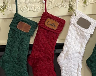 May include: Three knitted Christmas stockings hanging from a fireplace mantel. The stockings are green, red, and white. The red stocking has the name "Carter" on it.