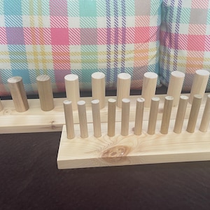 May include: Two unfinished wooden peg racks. One rack has angled pegs, the other has vertical pegs. The racks are made of light-colored wood and are set against a plaid pillow background.