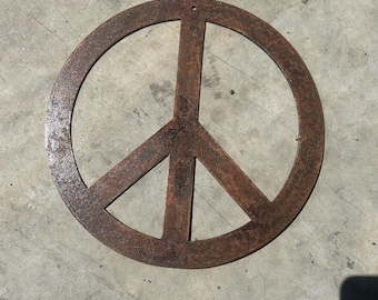 Op de afbeelding: Een roestig metalen vredesteken met een ronde vorm en een gat bovenaan om op te hangen.