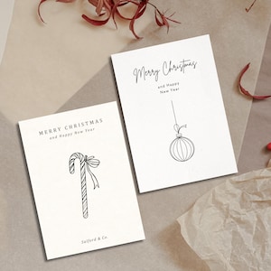 K&ouml;nnte beinhalten: Zwei wei&szlig;e Gru&szlig;karten mit schwarzen Strichzeichnungen eines Zuckerstabs und eines Weihnachtsbaumanh&auml;ngers. Der Text auf den Karten lautet "Frohe Weihnachten und ein gl&uuml;ckliches neues Jahr". Eine Karte tr&auml;gt den Text "Salford & Co."