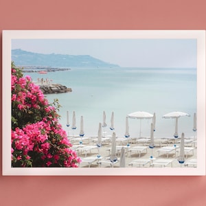 Stampa artistica da parete con spiaggia mediterranea – Fiori di bouganville rosa e ombrelloni da spiaggia – Poster fotografico di viaggio costiero