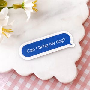 May include: A rectangular sticker with rounded corners featuring a blue background and a white speech bubble tail on the right side. The text "Can I bring my dog?" is printed in white, sans-serif capital and lowercase letters across the center.
