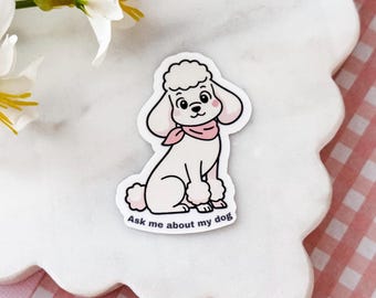 May include: A die-cut sticker featuring a white poodle with a pink neckerchief and pink cheeks. The poodle is sitting and has a curly topknot and leg puffs. The text "Ask me about my dog" is printed in black at the bottom of the sticker design.