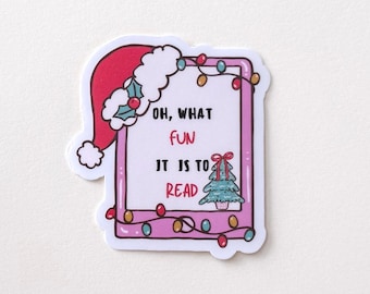 May include: A sticker with a pink border and the text "OH, WHAT FUN IT IS TO READ." A Santa hat is on the top left. A small Christmas tree is on the bottom right. The sticker is decorated with Christmas lights.