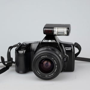 May include: A black Minolta Dynax 3000i film camera with a built-in flash and a black strap.