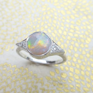 May include: A silver ring with a round opal gemstone and small diamonds on the band.