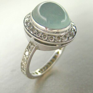 May include: A silver ring with a large, light blue gemstone surrounded by a halo of smaller, clear gemstones.