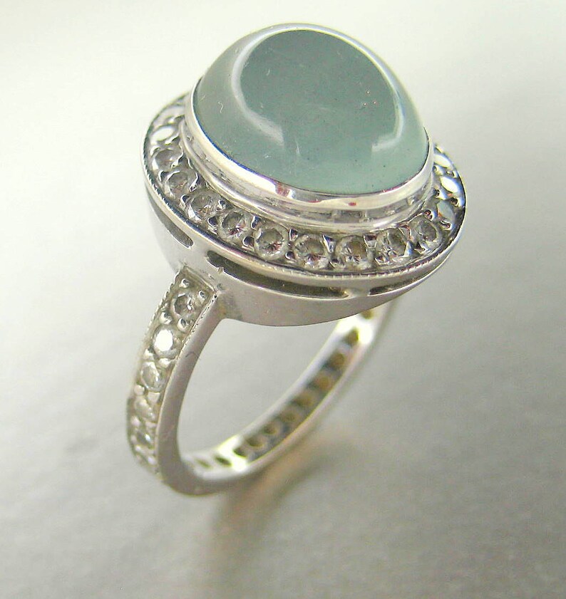 May include: A silver ring with a large, light blue gemstone surrounded by a halo of smaller, clear gemstones.