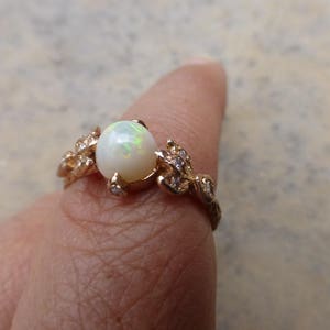 May include: A gold ring with a white opal gemstone and small clear stones set in a leaf design.