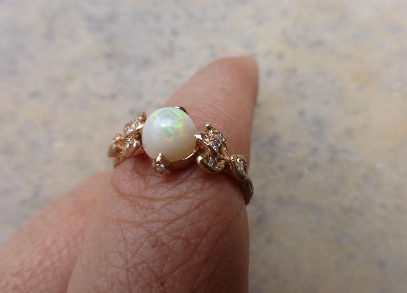 May include: A gold ring with a white opal gemstone and small clear stones set in a leaf design.