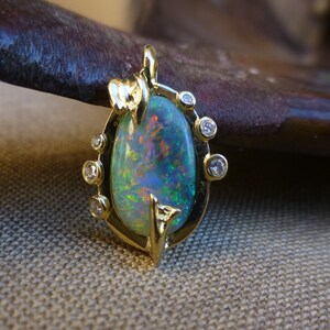 May include: A gold pendant featuring a large oval opal with a green, blue, and red iridescent sheen. The opal is surrounded by a gold setting with small diamonds.