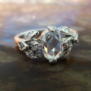 May include: A silver ring with a large, clear, oval-shaped gemstone surrounded by smaller, clear gemstones set in a leaf design.
