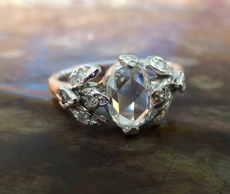 May include: A silver ring with a large, clear, oval-shaped gemstone surrounded by smaller, clear gemstones set in a leaf design.